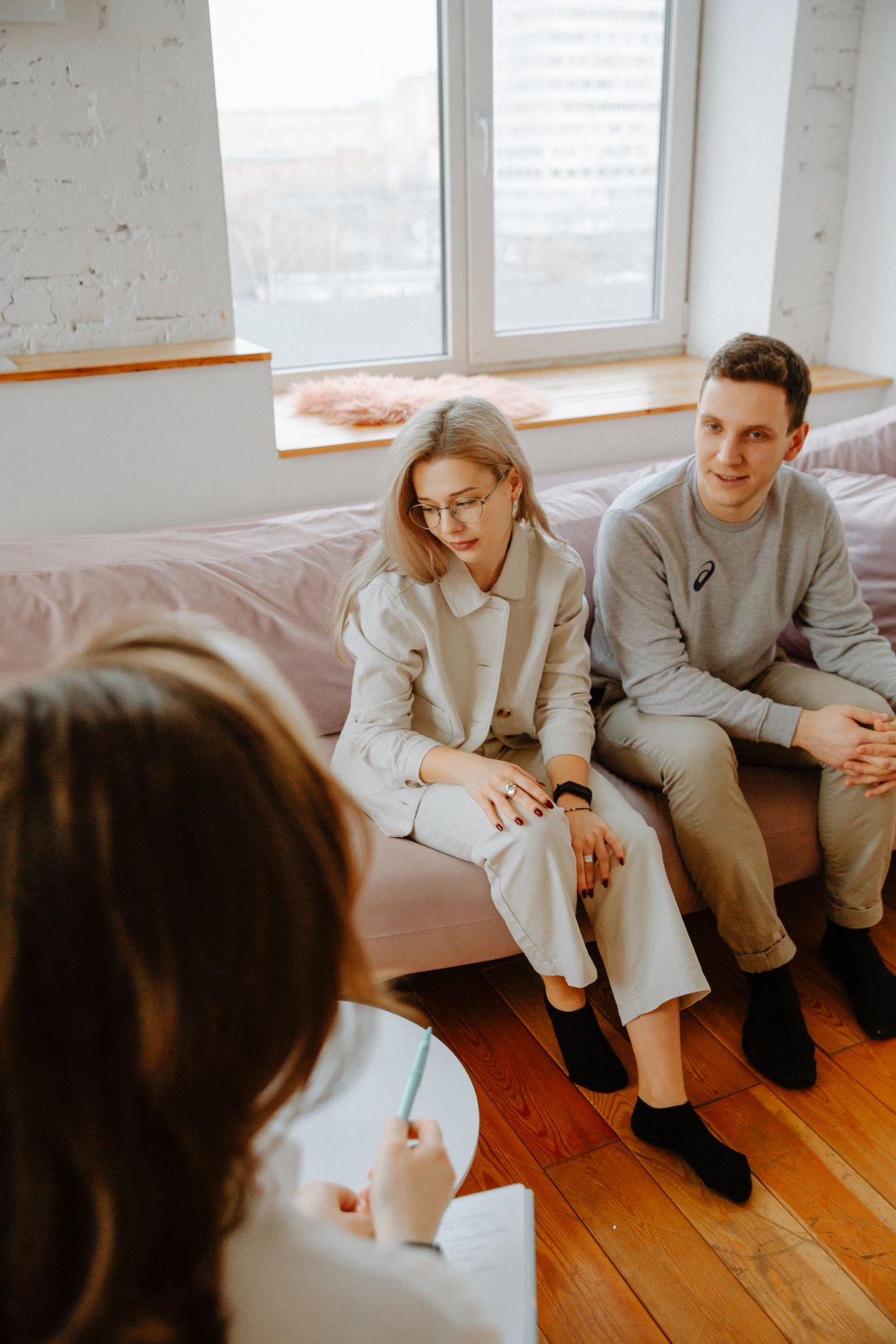 A couple seated together on the couch, mid-conversation in a warm therapy room